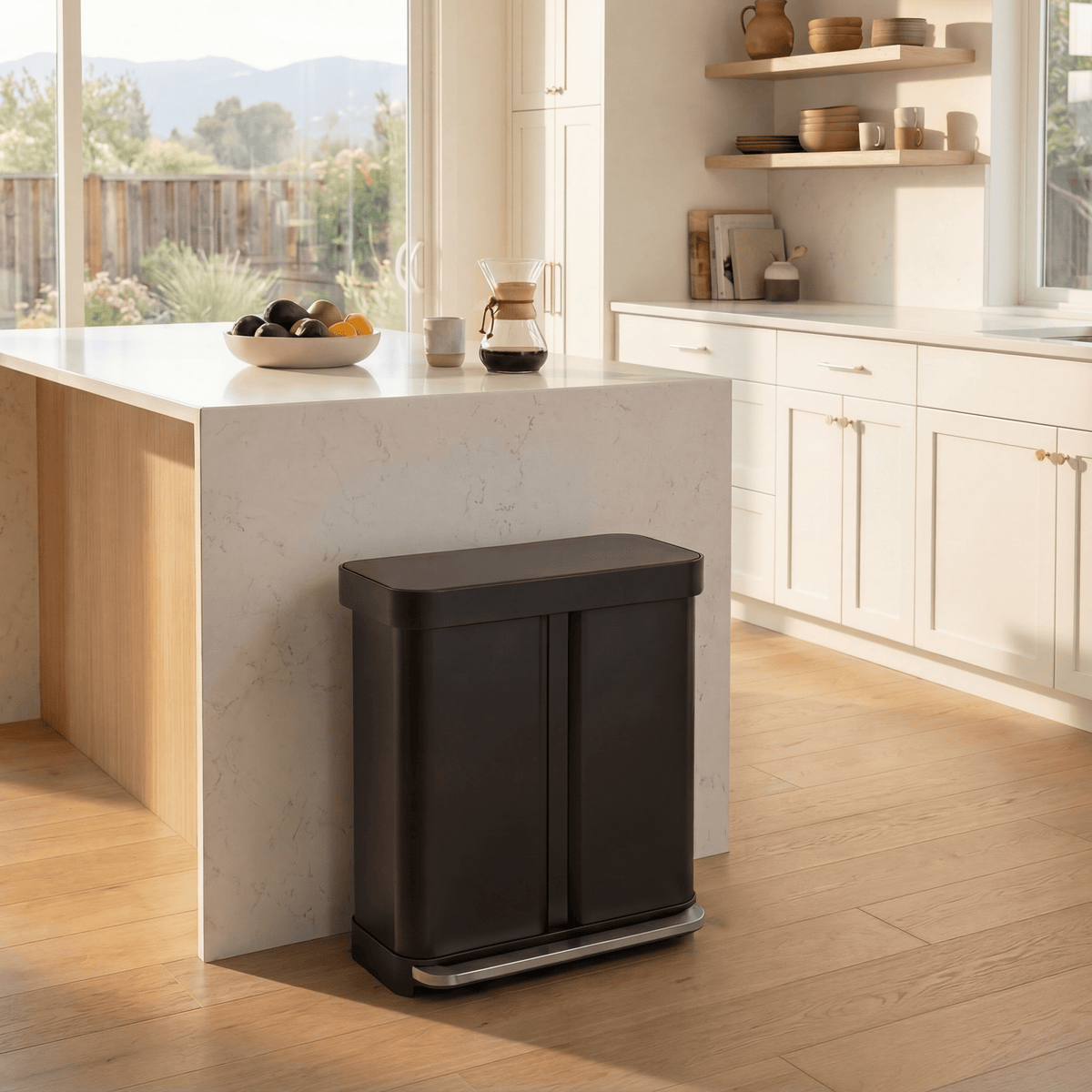 Simplehuman's Matte Black 58L Step Recycler in a simple, classic styled kitchen with white and marble accents and a few house hold appliances on the shelves and countertop.